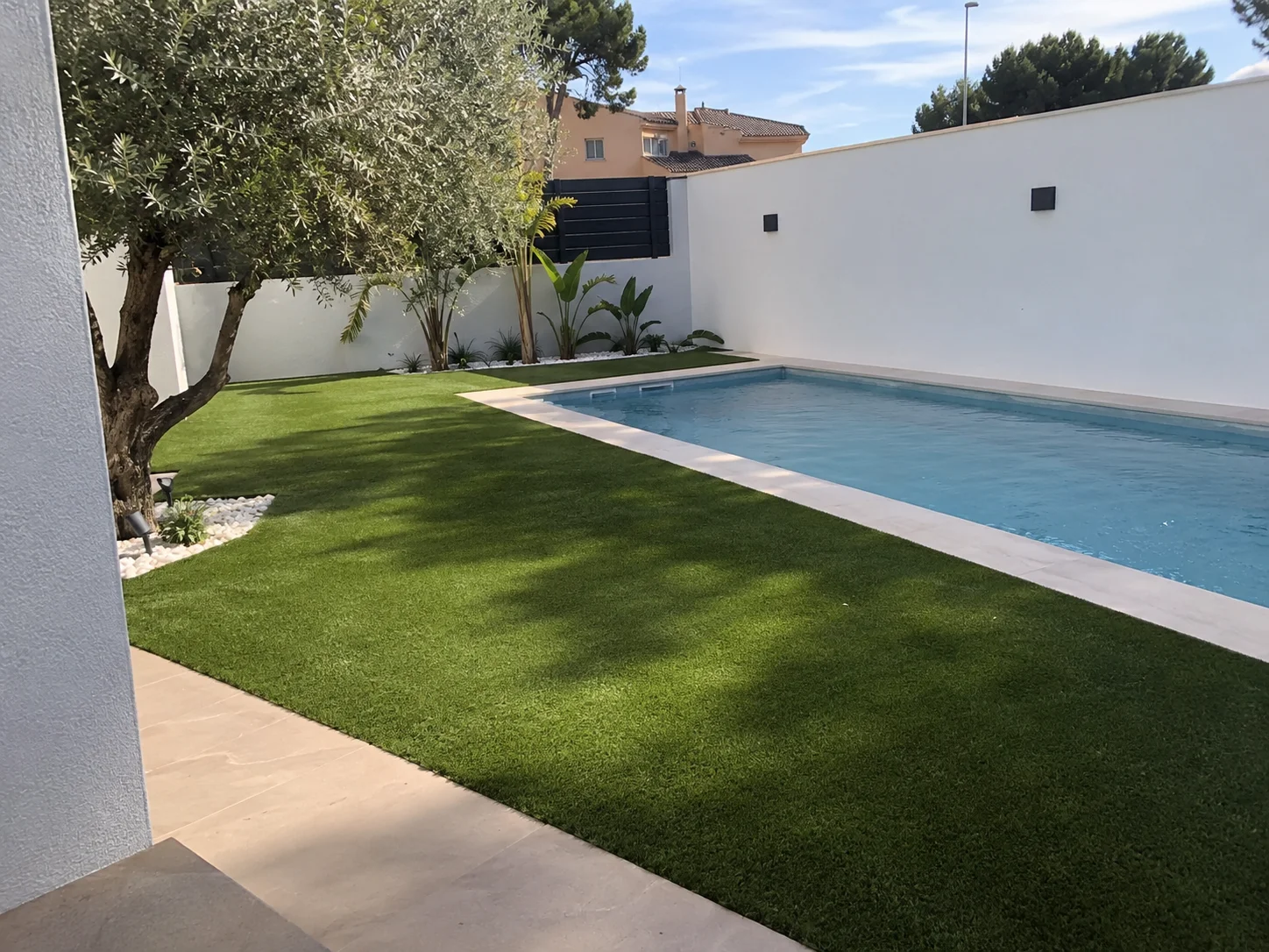 Zona de piscina rodeada de césped artificial y árboles