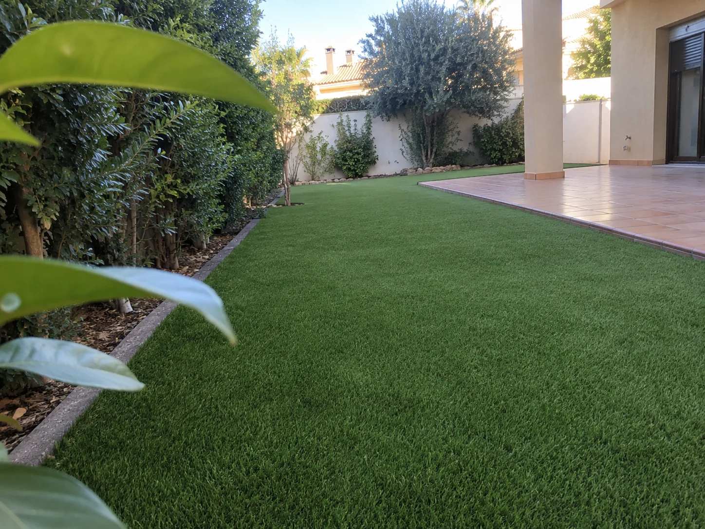 Jardín alargado con césped artificial junto a vegetación