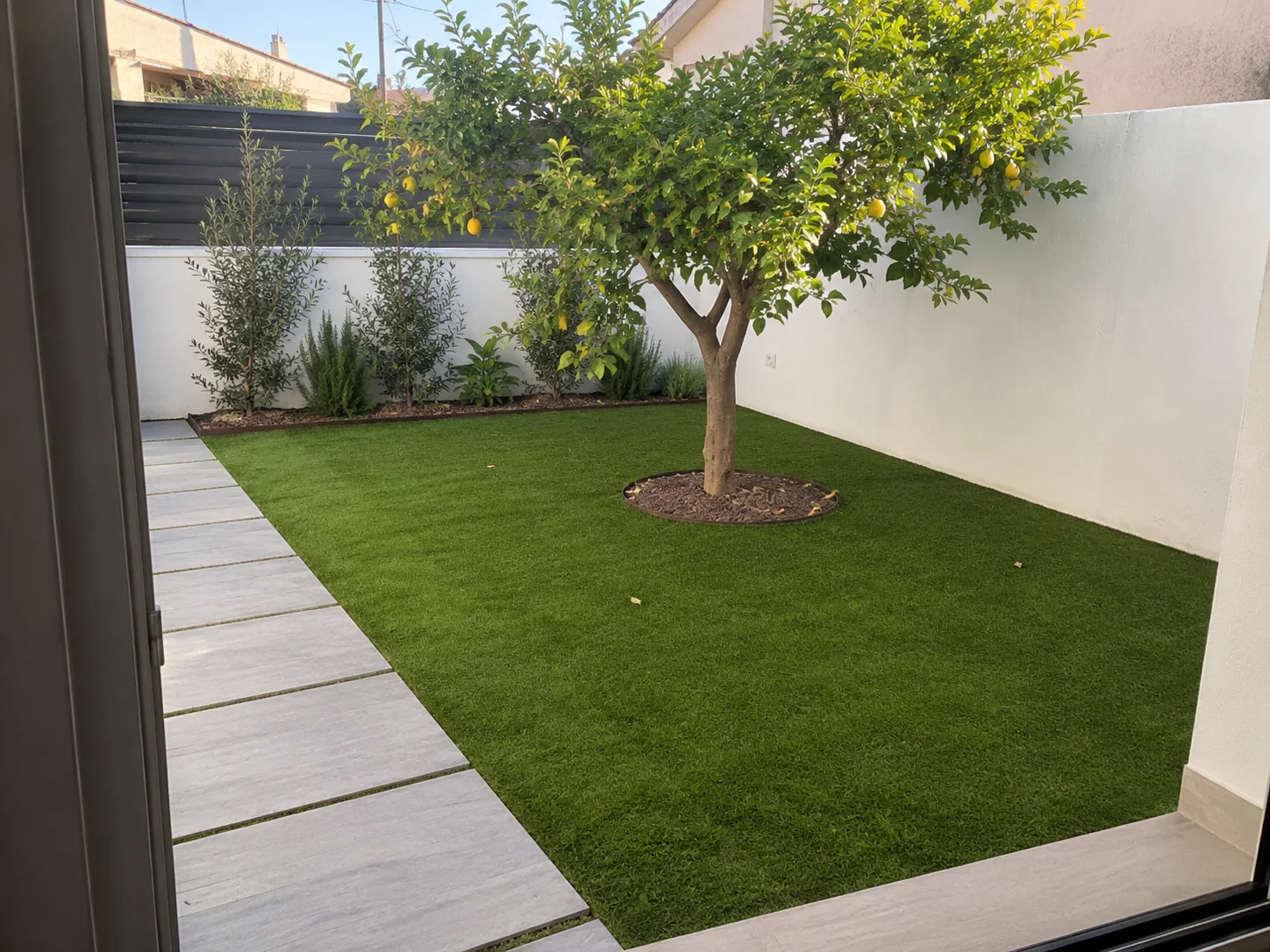 Jardín rectangular con césped artificial alrededor de un árbol