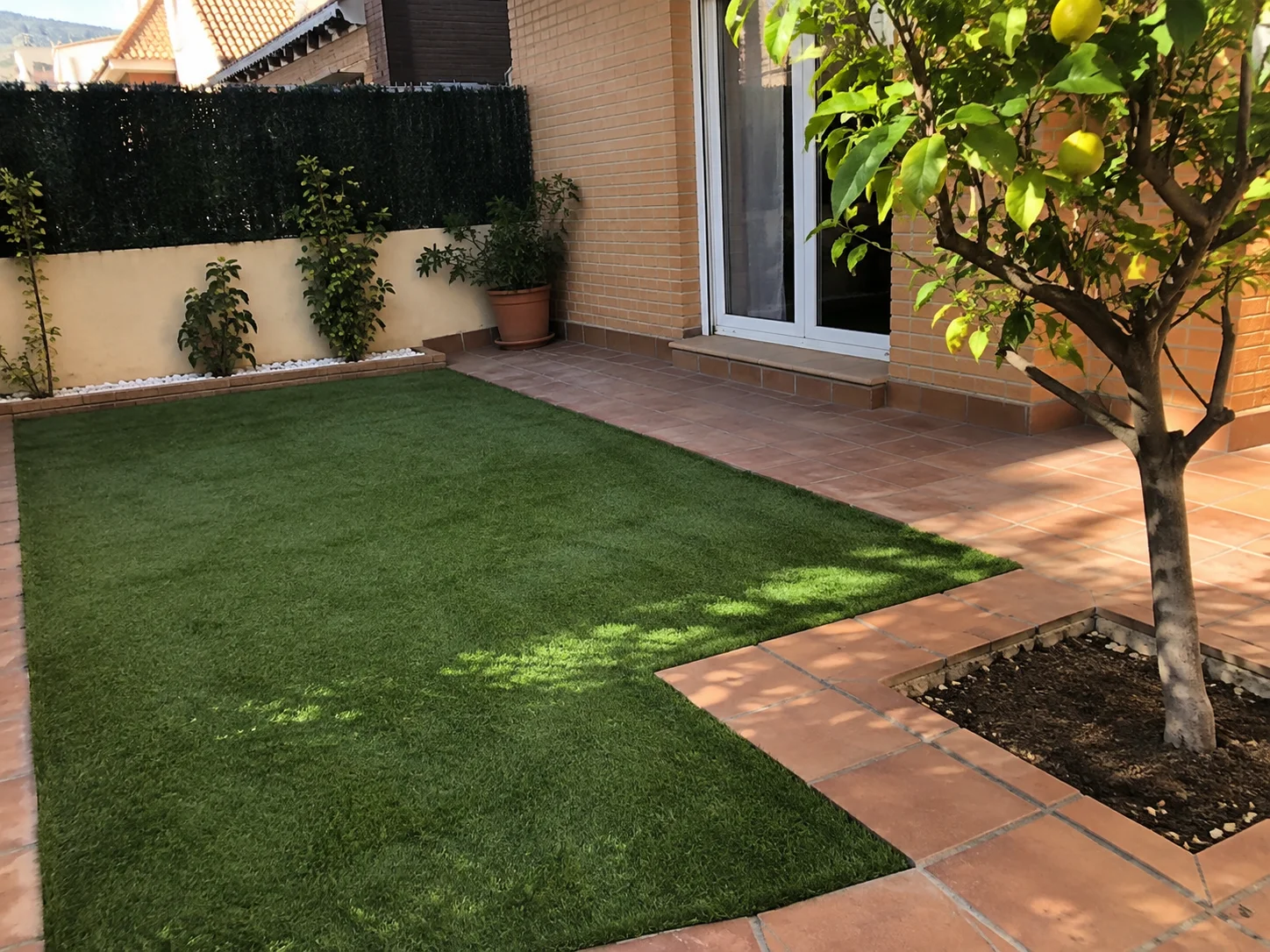 Patio con césped artificial y árbol integrado en el pavimento