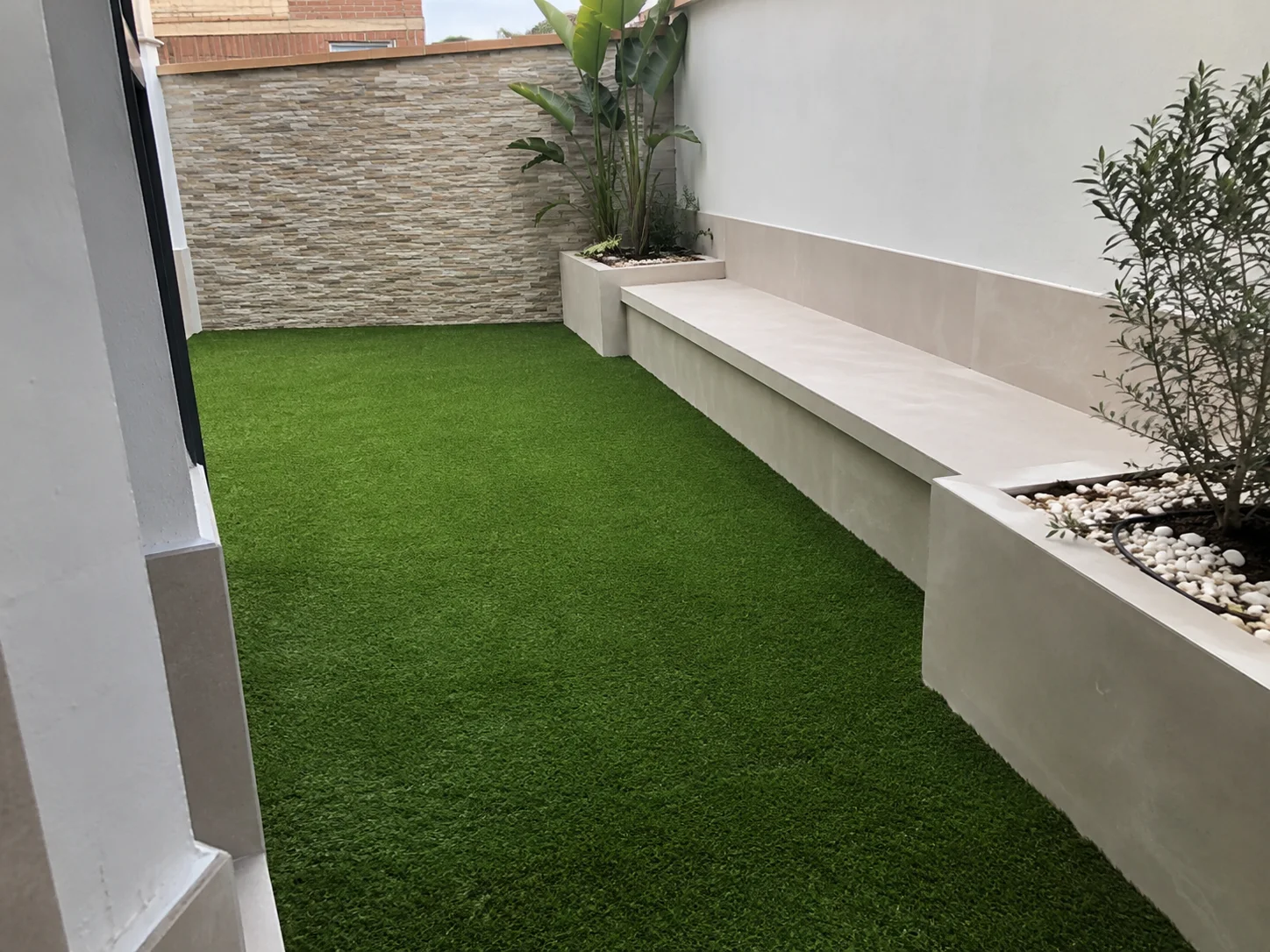 Patio estrecho con césped artificial y banco de obra