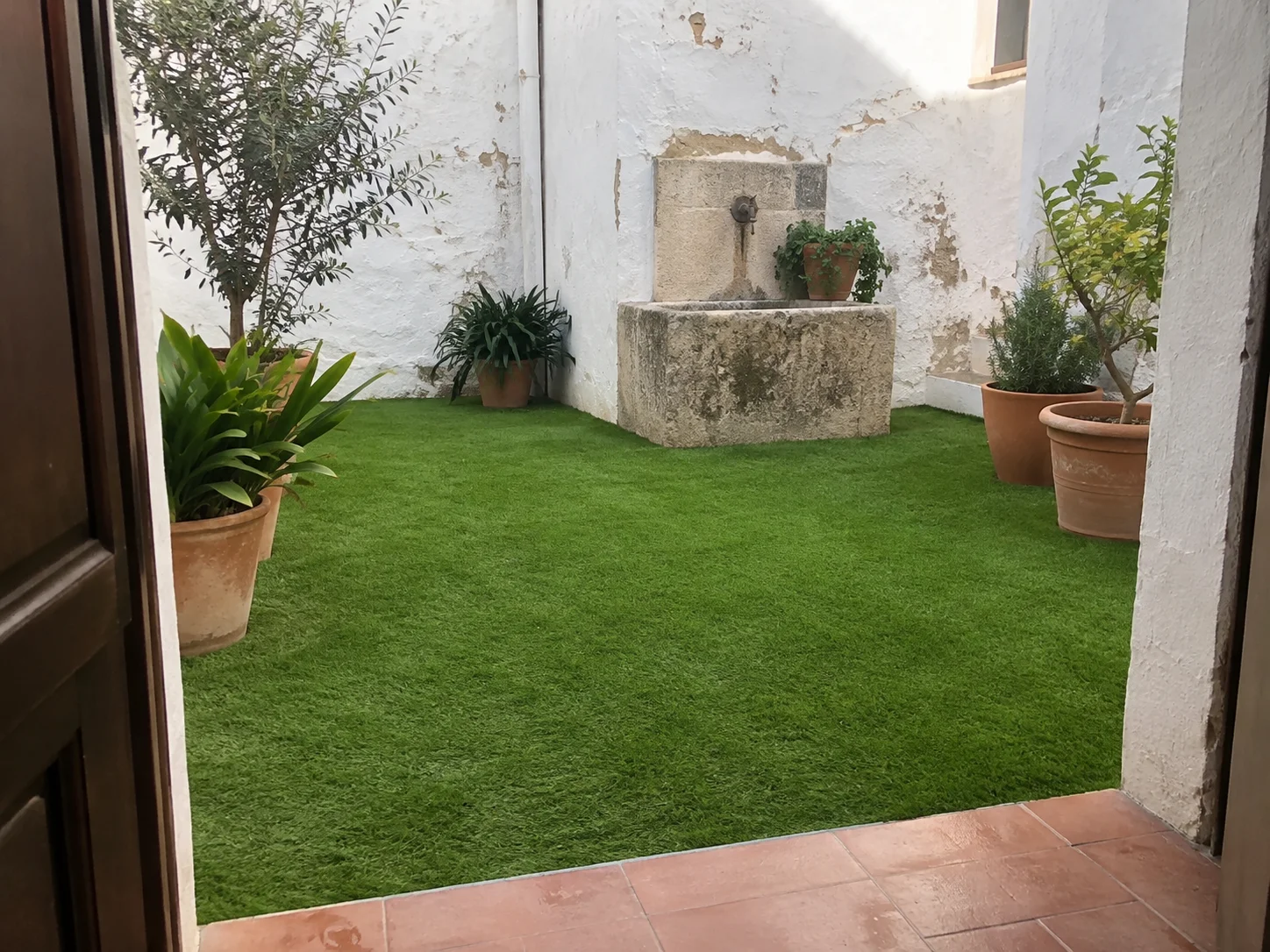 Patio con césped artificial, macetas y fuente de piedra